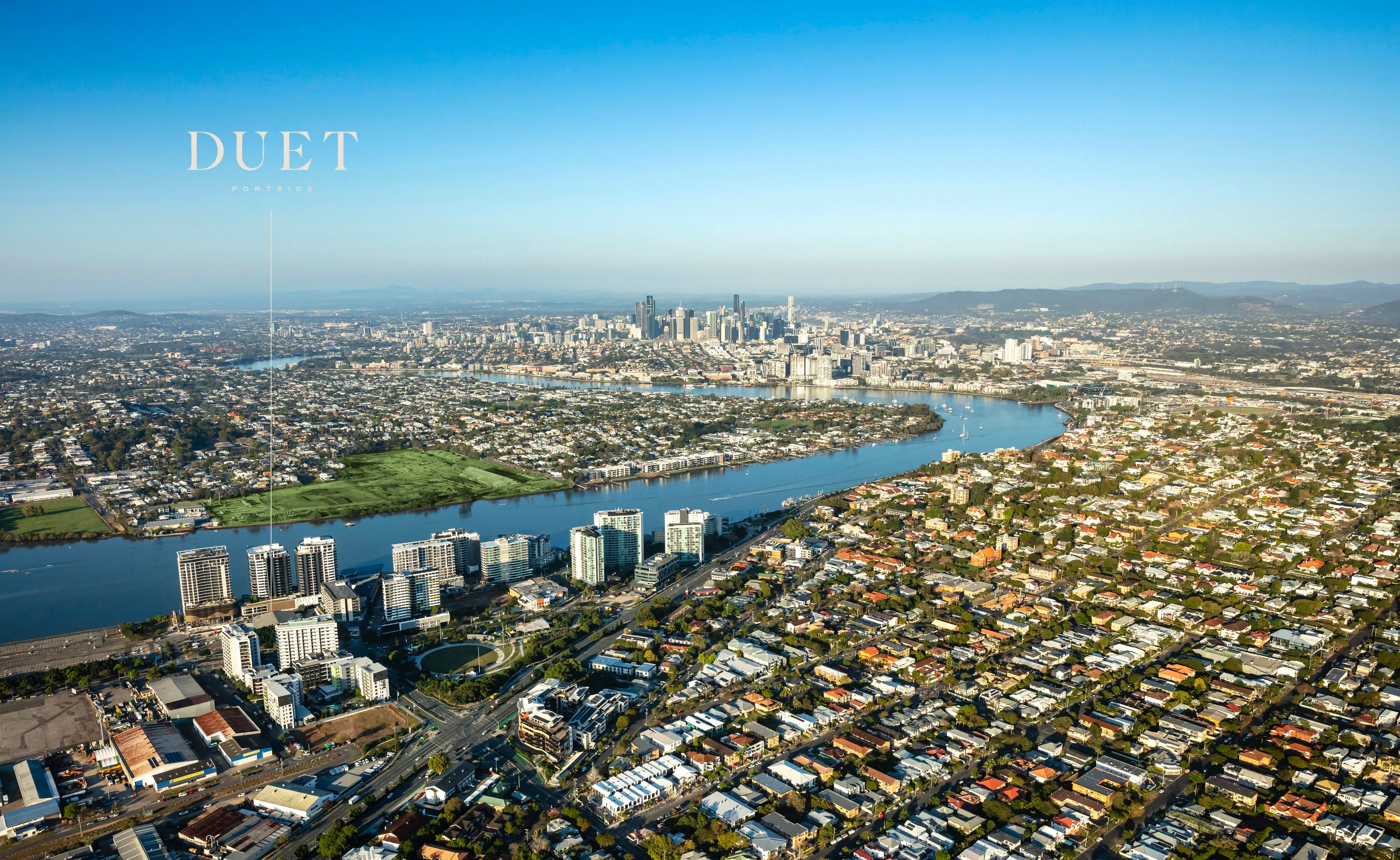 Aerial photograph of the Hamilton reach of the Brisbane River at dawn, the DUET Portside site marked against the city skyline beyond